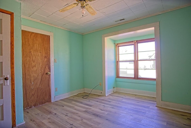 unfurnished room with wood finished floors, visible vents, baseboards, a ceiling fan, and crown molding