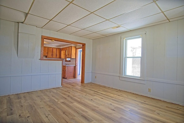 empty room featuring a drop ceiling, wood finished floors, and a decorative wall