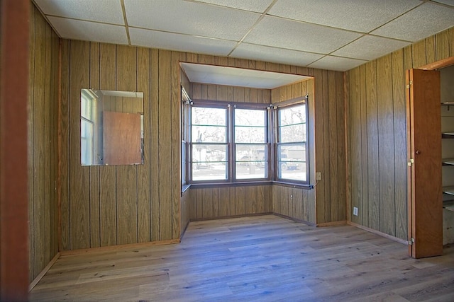 spare room with a paneled ceiling, wooden walls, and wood finished floors