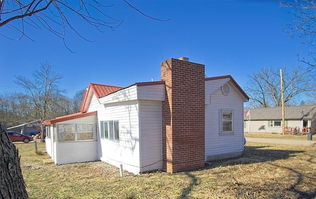 view of side of property featuring a chimney, metal roof, and a lawn