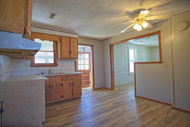 kitchen with brown cabinets, light wood finished floors, light countertops, a sink, and under cabinet range hood