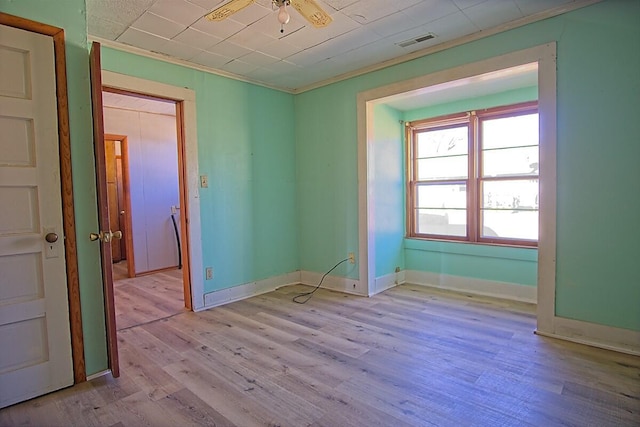 empty room featuring light wood finished floors, baseboards, visible vents, ceiling fan, and ornamental molding