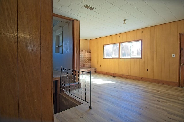 spare room featuring wooden walls, wood finished floors, visible vents, and baseboards