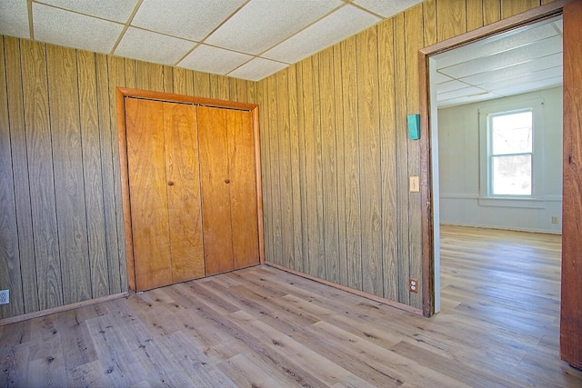 empty room with wood walls, a drop ceiling, and wood finished floors