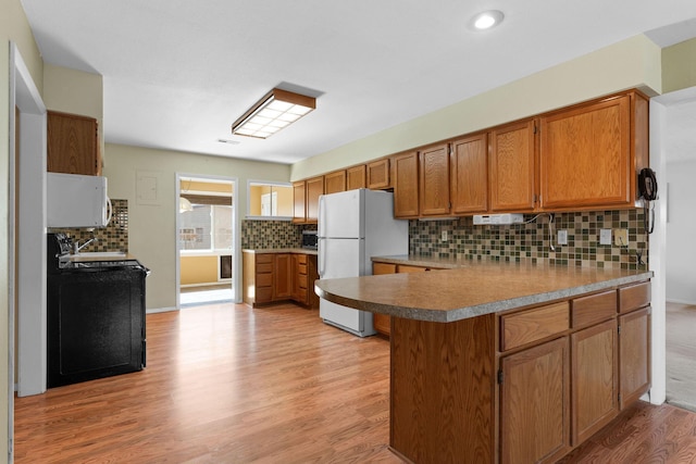 kitchen featuring white appliances, brown cabinets, a peninsula, light wood-type flooring, and a sink