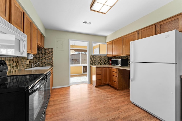 kitchen featuring light wood finished floors, visible vents, brown cabinetry, black appliances, and a sink