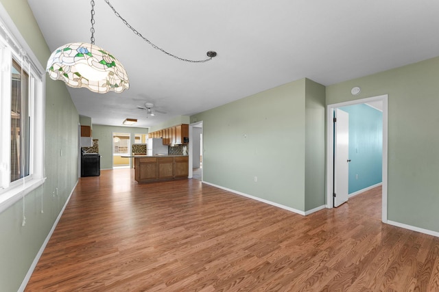 unfurnished living room featuring ceiling fan, wood finished floors, and baseboards