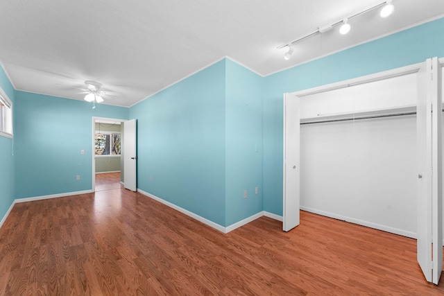 unfurnished bedroom featuring baseboards, ceiling fan, wood finished floors, crown molding, and a closet