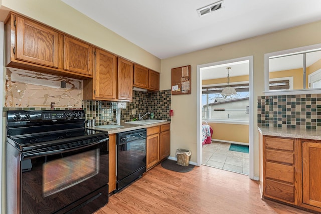 kitchen with a sink, visible vents, light countertops, brown cabinets, and black appliances