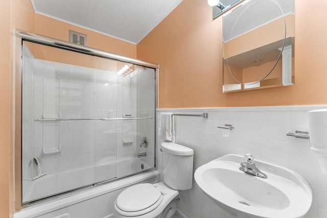 bathroom featuring enclosed tub / shower combo, toilet, a sink, tile walls, and wainscoting