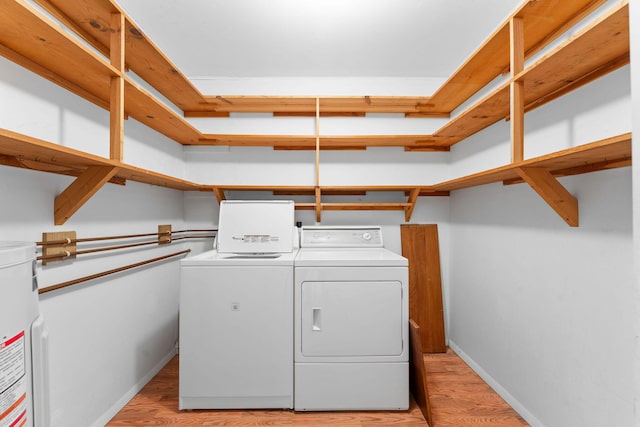 clothes washing area featuring light wood-style flooring, water heater, baseboards, and washing machine and clothes dryer