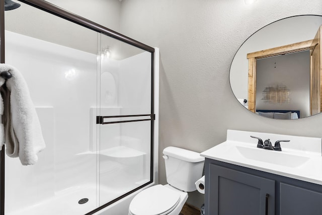 bathroom featuring toilet, a shower with door, a textured wall, and vanity