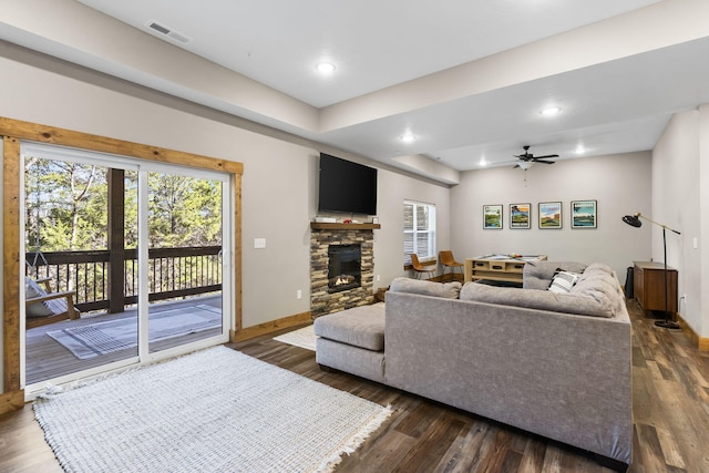 living area with dark wood-type flooring, visible vents, a stone fireplace, and baseboards