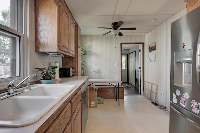 kitchen with wallpapered walls, appliances with stainless steel finishes, brown cabinets, light countertops, and a sink