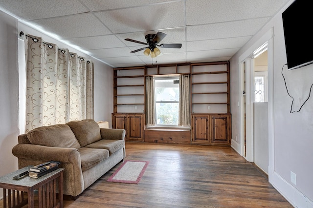 living room featuring a paneled ceiling, ceiling fan, baseboards, and wood finished floors