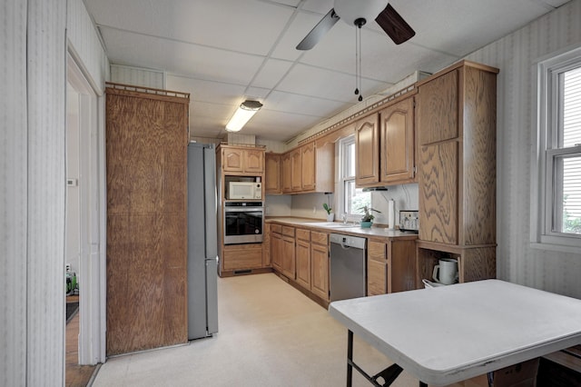 kitchen with light countertops, appliances with stainless steel finishes, a ceiling fan, a sink, and wallpapered walls