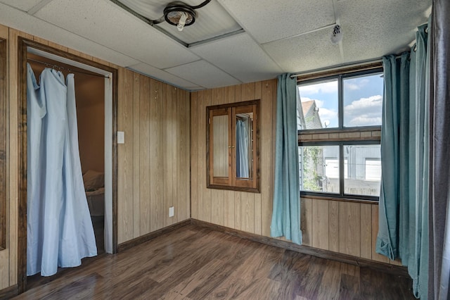 unfurnished room with wood walls, dark wood-style flooring, a drop ceiling, and baseboards