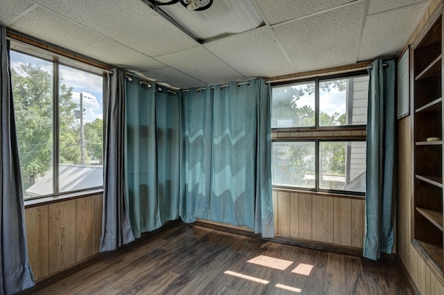 unfurnished room with wood walls, dark wood-style flooring, and a drop ceiling