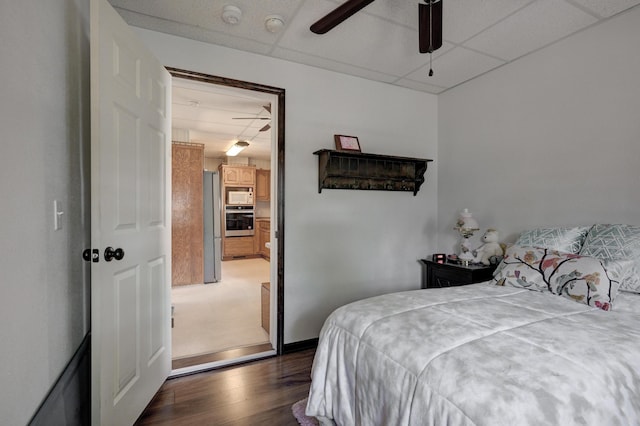 bedroom featuring freestanding refrigerator, dark wood-style flooring, a drop ceiling, and ceiling fan