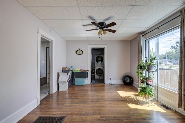 interior space with stacked washer and dryer, baseboards, a drop ceiling, and wood finished floors