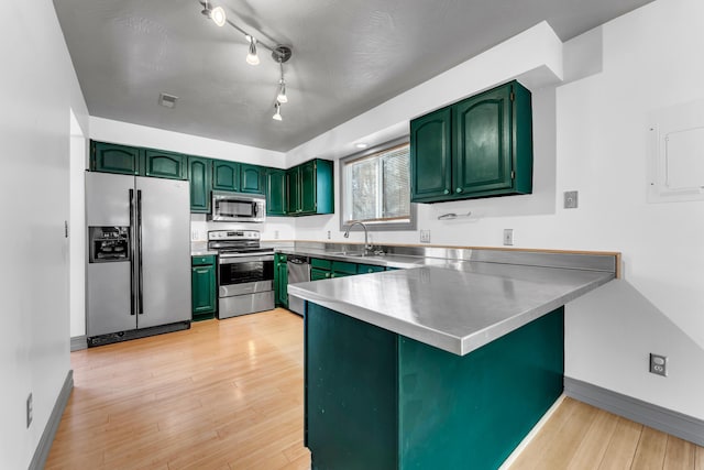 kitchen featuring a peninsula, a sink, appliances with stainless steel finishes, light wood-type flooring, and green cabinetry