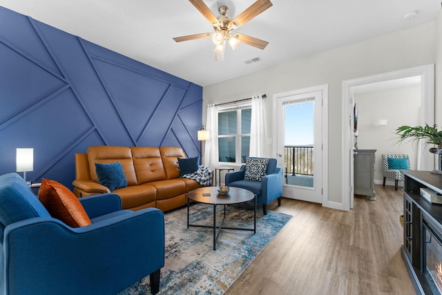 living area with baseboards, wood finished floors, visible vents, and a ceiling fan