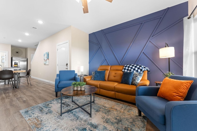 living area featuring recessed lighting, visible vents, a decorative wall, wood finished floors, and baseboards