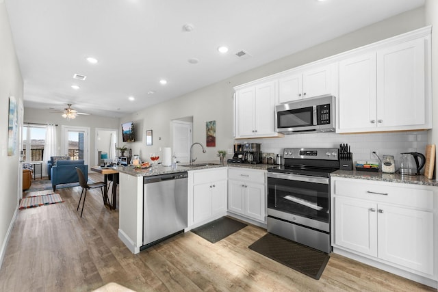 kitchen with stainless steel appliances, a peninsula, a sink, white cabinets, and open floor plan