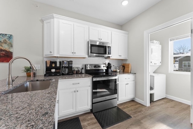 kitchen featuring a sink, appliances with stainless steel finishes, stacked washing maching and dryer, backsplash, and light wood finished floors