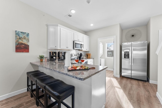 kitchen featuring light wood-style flooring, a peninsula, light stone countertops, stainless steel appliances, and white cabinetry