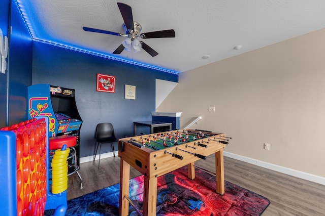 rec room with ceiling fan, a textured ceiling, wood finished floors, and baseboards