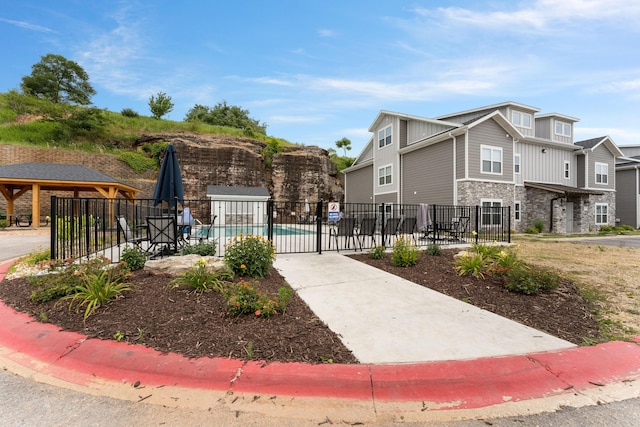 view of front of house featuring board and batten siding, stone siding, fence, and a community pool