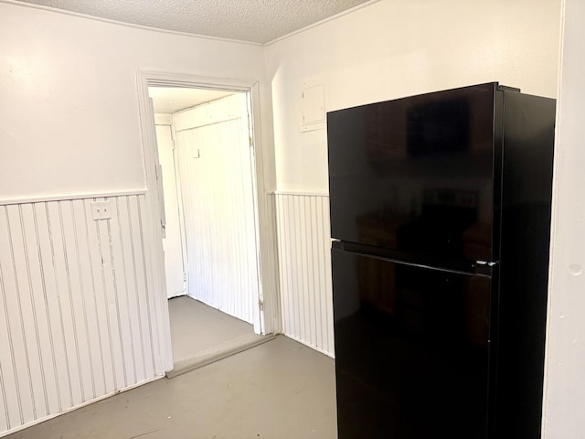 corridor with a textured ceiling, concrete floors, and wainscoting