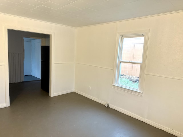 spare room with finished concrete flooring, crown molding, and baseboards