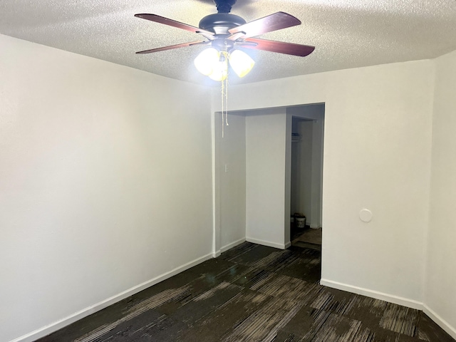 unfurnished room with a textured ceiling, ceiling fan, dark wood finished floors, and baseboards