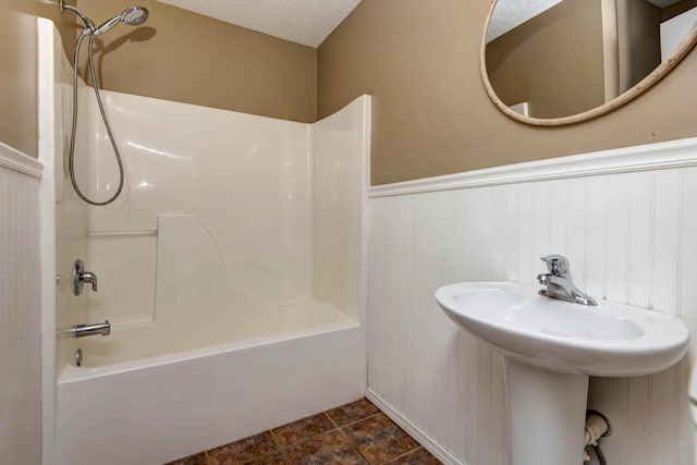 bathroom featuring shower / bath combination, a sink, a textured ceiling, and wainscoting