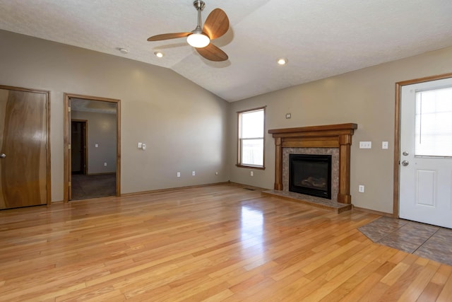 unfurnished living room with light wood-style floors, lofted ceiling, a healthy amount of sunlight, and a glass covered fireplace