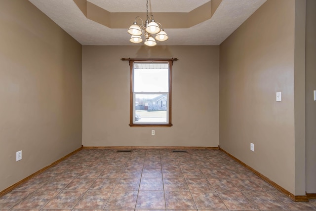 empty room featuring a textured ceiling, a tray ceiling, baseboards, and an inviting chandelier