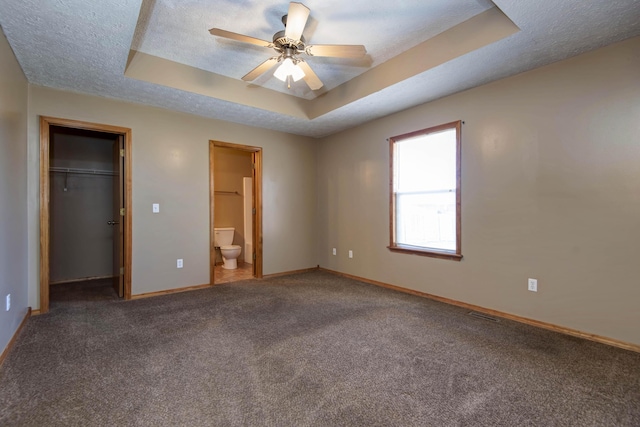 unfurnished bedroom with a tray ceiling, a walk in closet, carpet flooring, a textured ceiling, and baseboards