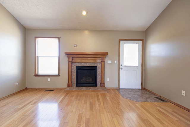 unfurnished living room with baseboards, visible vents, a tile fireplace, light wood-style flooring, and a textured ceiling