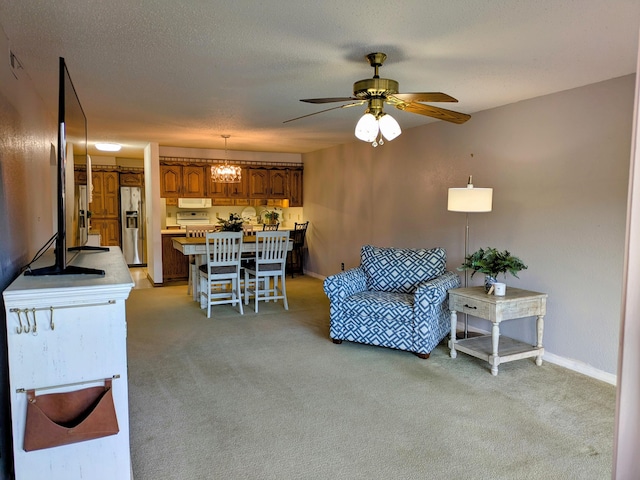 living area featuring light carpet, a ceiling fan, baseboards, and a textured ceiling