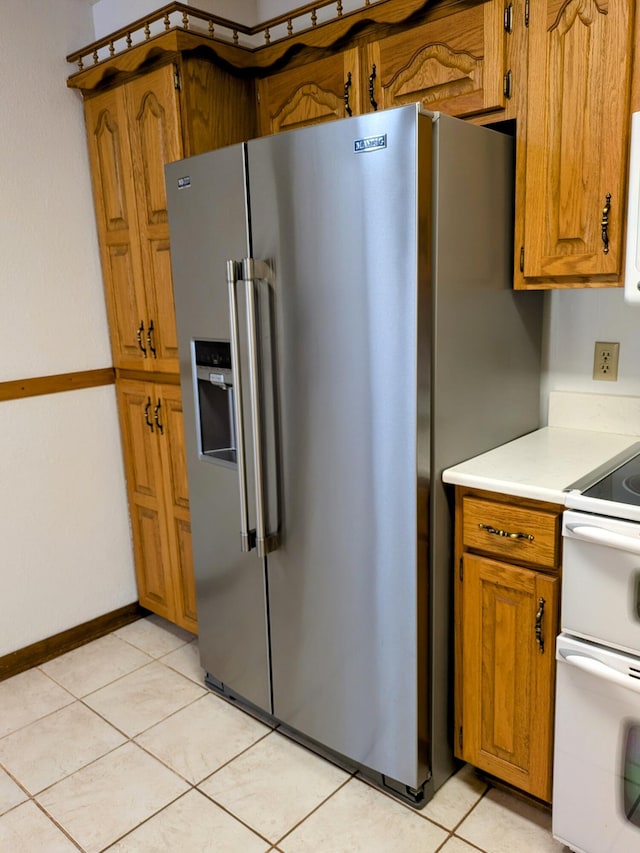 kitchen featuring light tile patterned floors, light countertops, brown cabinetry, white appliances, and baseboards