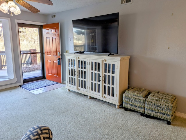 carpeted living area featuring a ceiling fan, visible vents, a textured ceiling, and baseboards