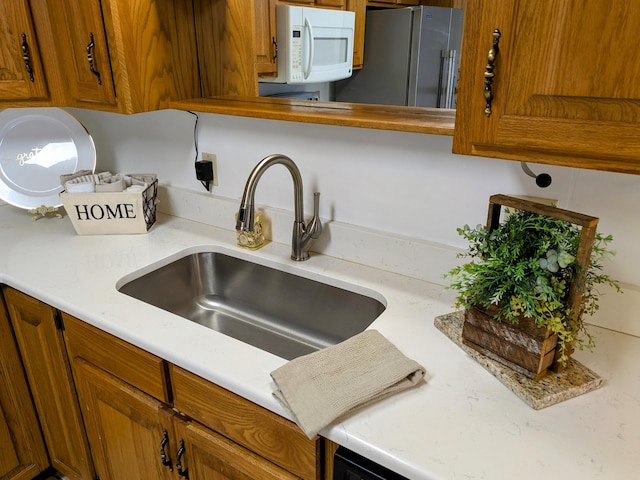 kitchen featuring white microwave, brown cabinets, a sink, and light countertops