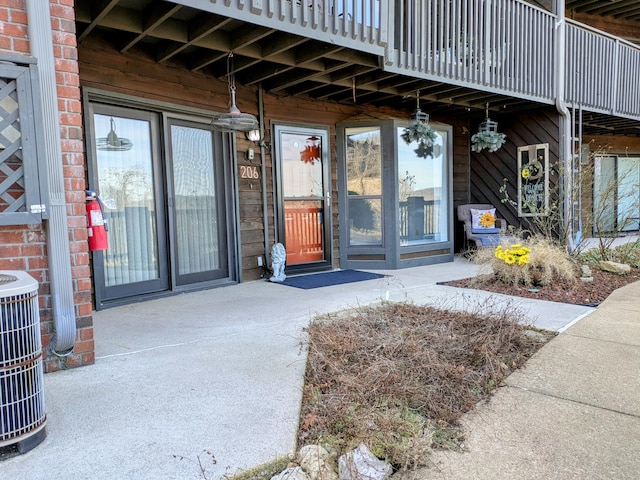 entrance to property with cooling unit, brick siding, and a balcony