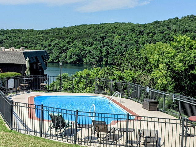 pool featuring a forest view, a patio area, and fence