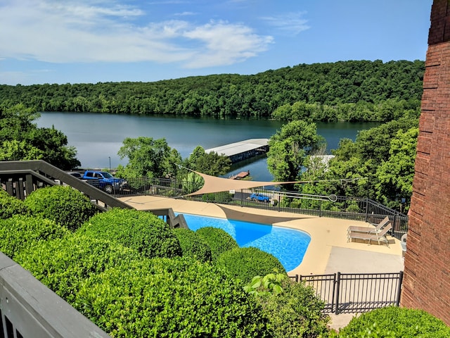 pool with a water view, a patio area, a forest view, and fence