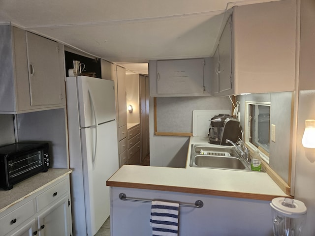 kitchen with a toaster, light countertops, a sink, and freestanding refrigerator