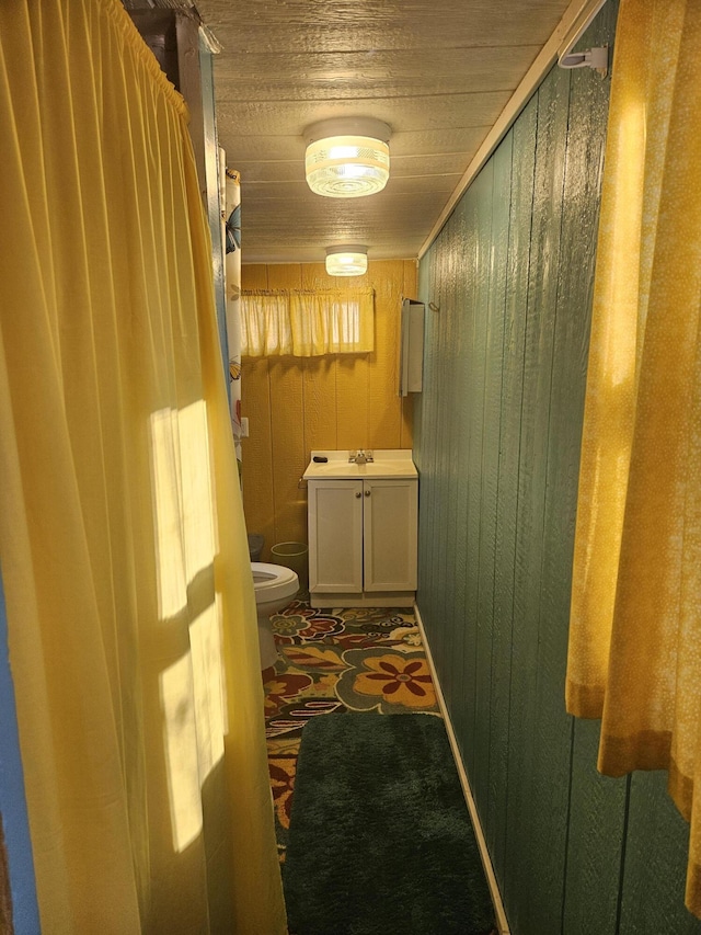 bathroom with toilet, wood walls, wood ceiling, and vanity