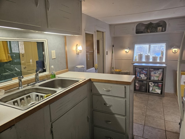 kitchen featuring gray cabinetry, a peninsula, a sink, light countertops, and tile patterned floors